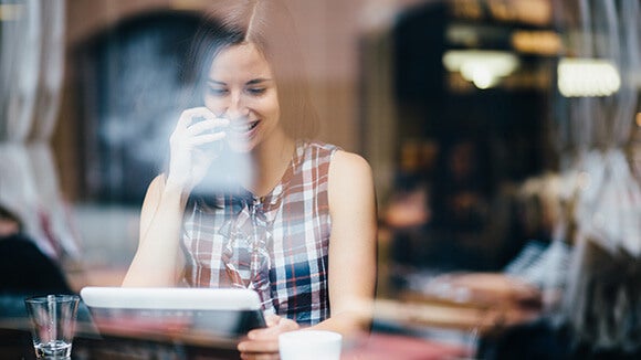 woman in coffee shop wearing a plaid shirt on tablet researching a new role